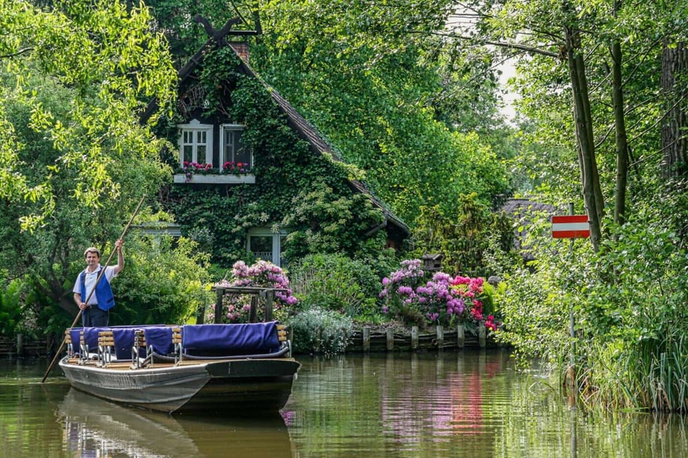 Andreas Schmidtchen stakt den Kahn durch ein Spreewald-Fließ vor einem reetgedeckten Hof